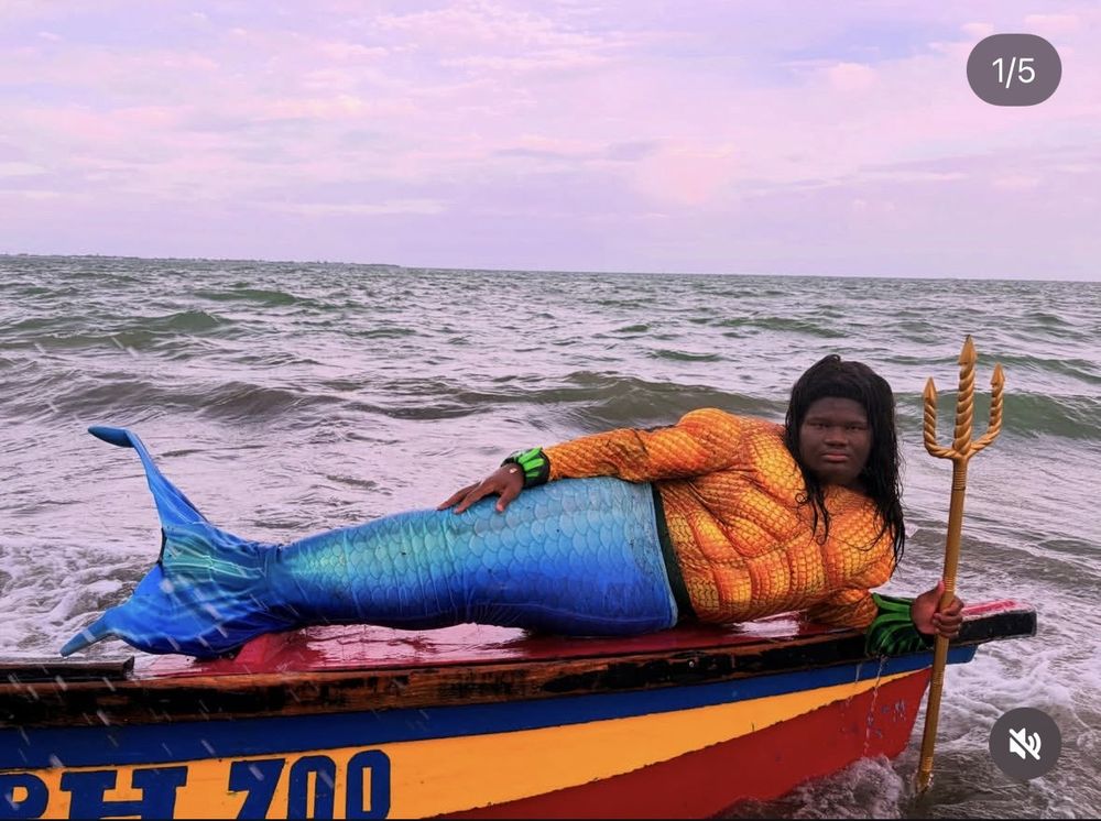 Lex in a mermaid tail and an orange scale top, lying on a fishing boat with a golden trident